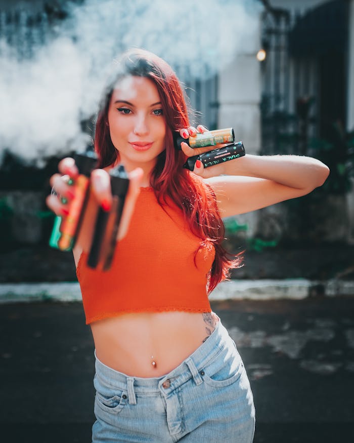 services-03 Confident woman with dyed red hair holding colorful vapes on a street, showcasing modern urban fashion.