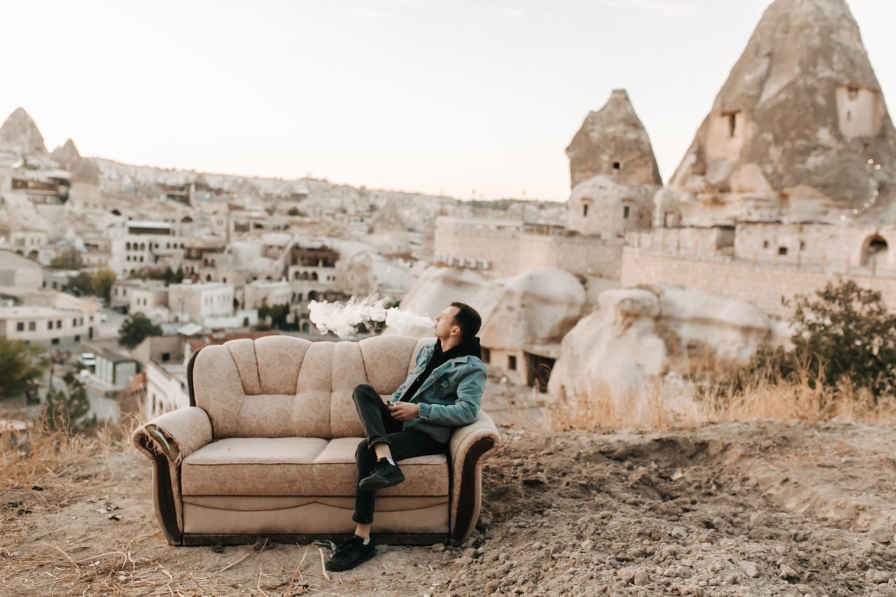 A man sits on a sofa while vaping, overlooking the unique landscape of Cappadocia, Turkey.