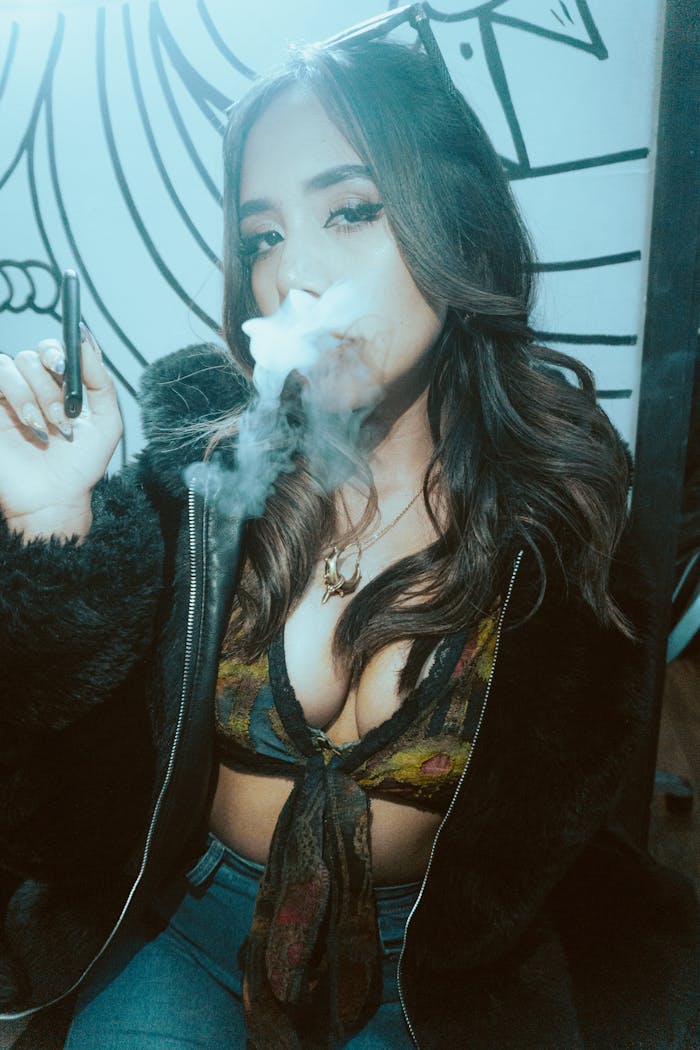 A fashionable woman vaping indoors, creating a cloud of smoke in a trendy environment.